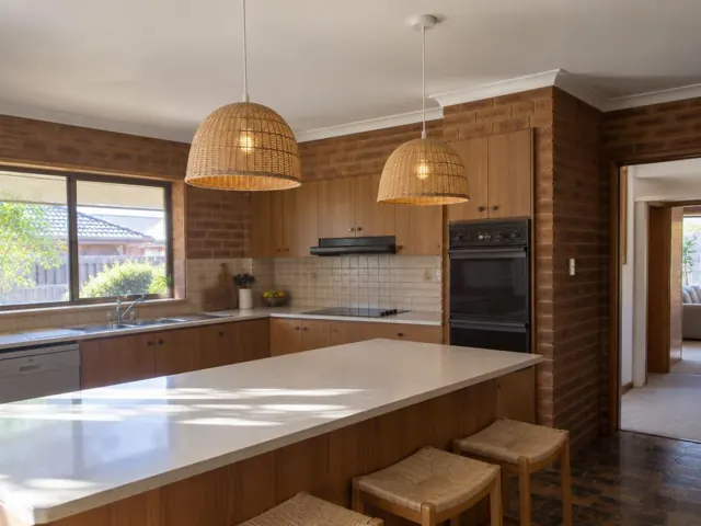 Two woven pendant lights over a kitchen island in a brick-walled home in Tenambit