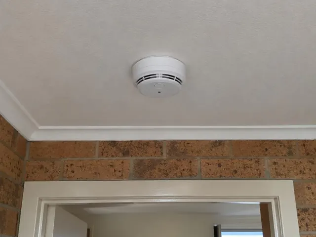 Ceiling smoke alarm above a doorway in a brick home interior in Ashtonfield